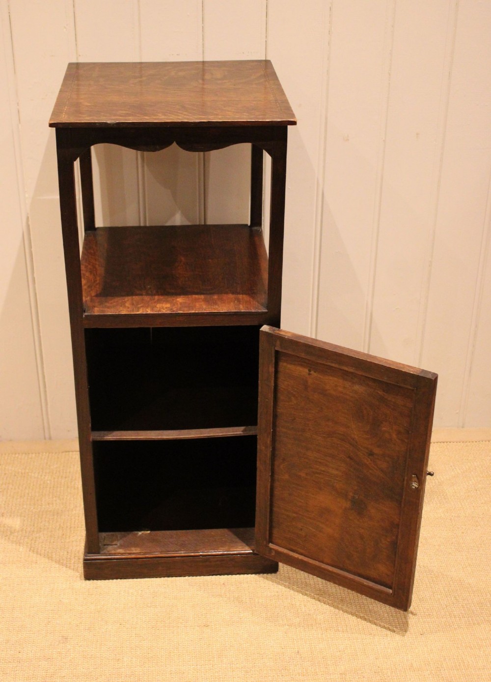 A dark oak Edwardian bedside cabinet with an open upper shelf, shaped apron, and a panelled single door below. View IV