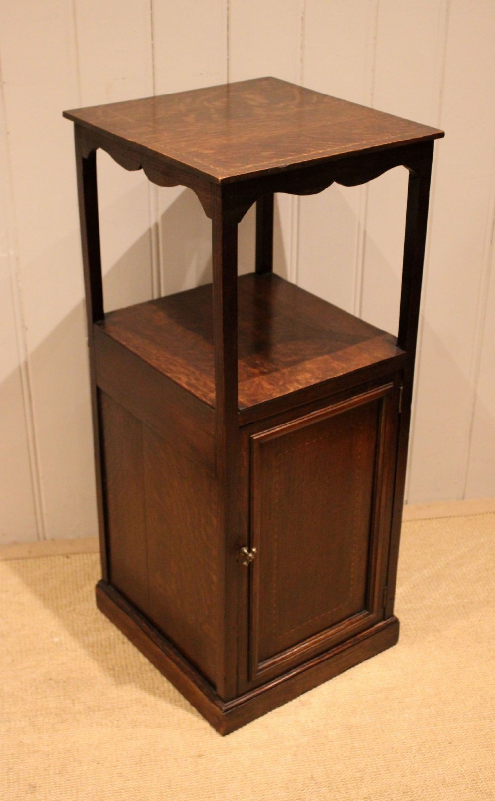 A dark oak Edwardian bedside cabinet with an open upper shelf, shaped apron, and a panelled single door below. View V