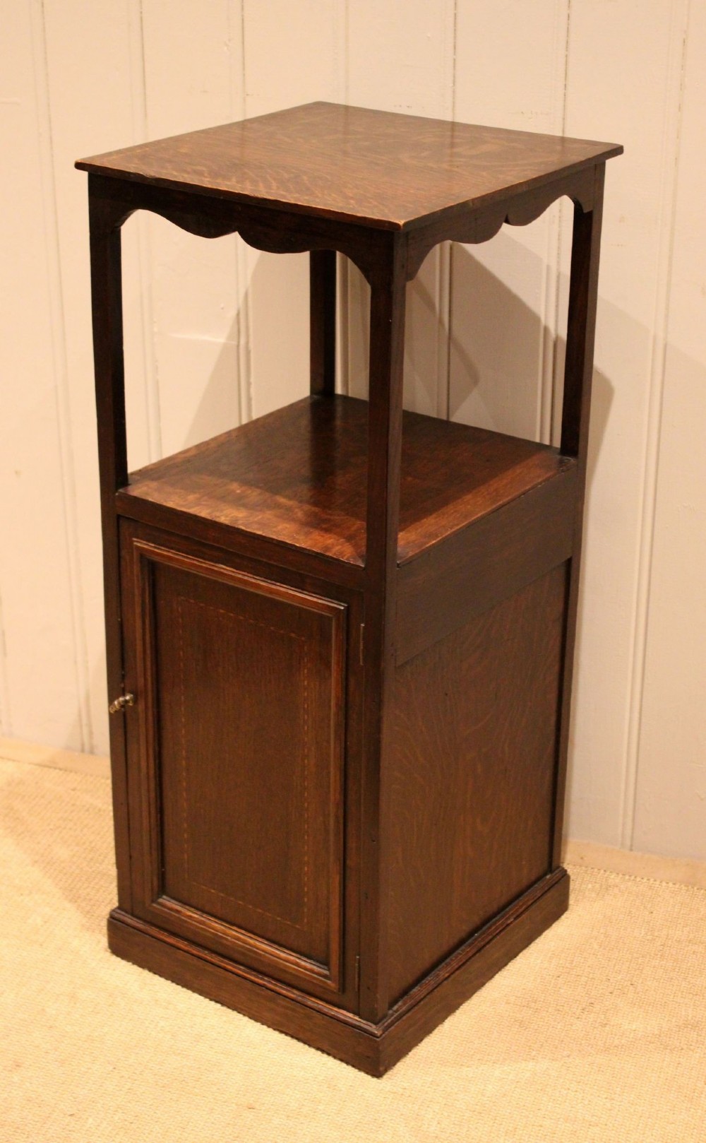 A dark oak Edwardian bedside cabinet with an open upper shelf, shaped apron, and a panelled single door below. View VI