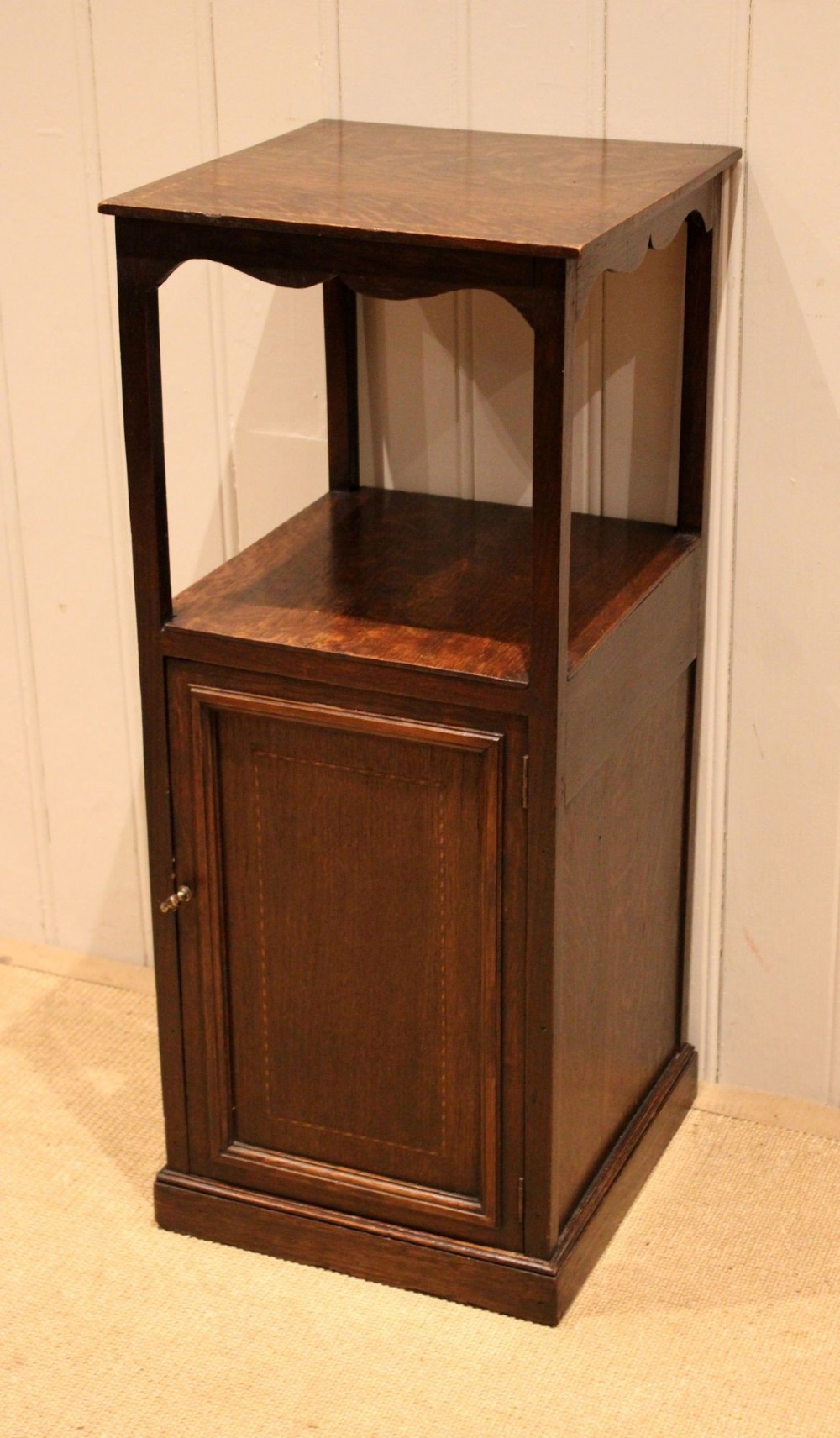 A dark oak Edwardian bedside cabinet with an open upper shelf, shaped apron, and a panelled single door below. View VII