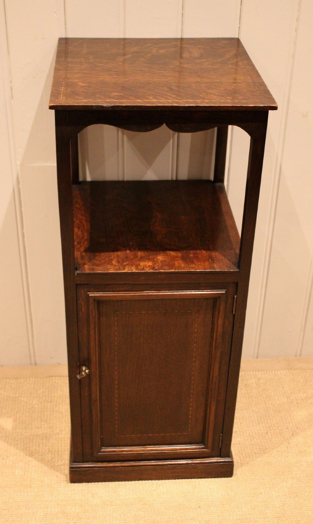 A dark oak Edwardian bedside cabinet with an open upper shelf, shaped apron, and a panelled single door below. View VIII