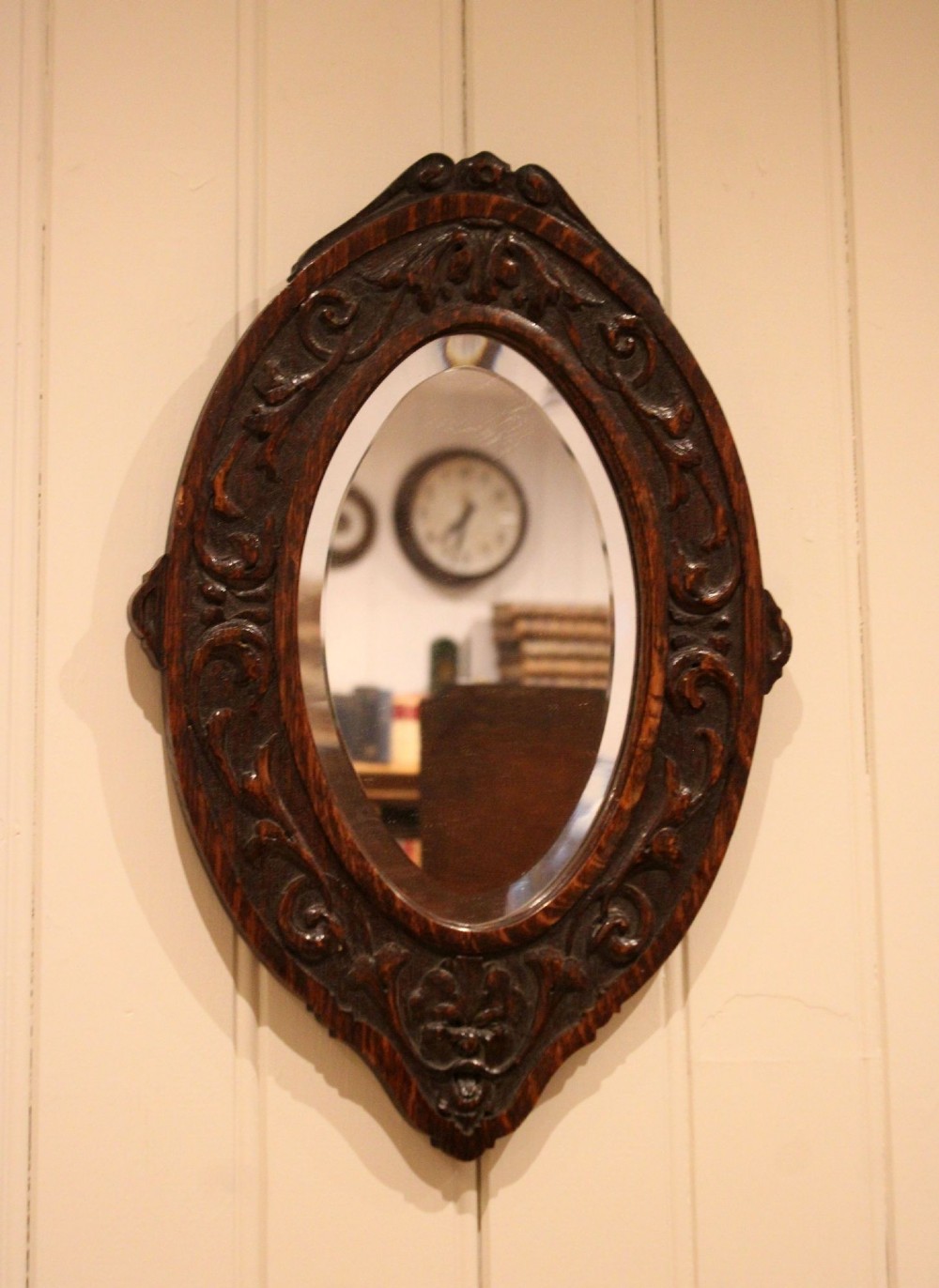 A small oval wall mirror featuring a heavily carved dark oak wooden frame with scroll motifs and a bevelled glass plate. View III