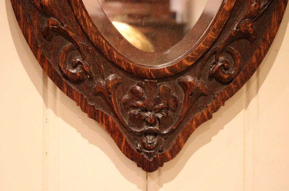 A small oval wall mirror featuring a heavily carved dark oak wooden frame with scroll motifs and a bevelled glass plate. View VI