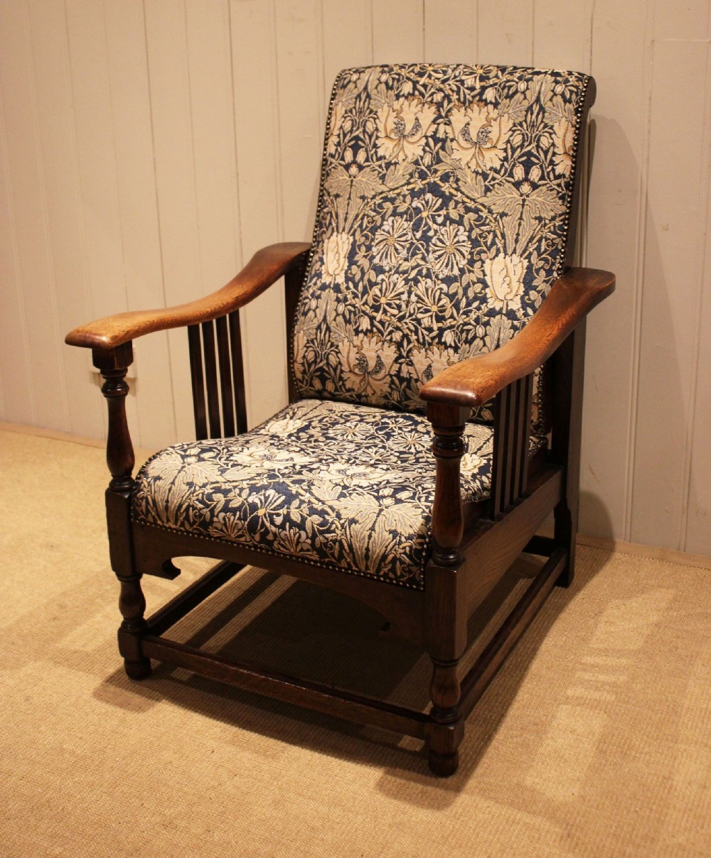 An Arts and Crafts oak reclining armchair featuring slatted sides, turned front legs, wide armrests, and floral pattern upholstery in blue and cream tones.