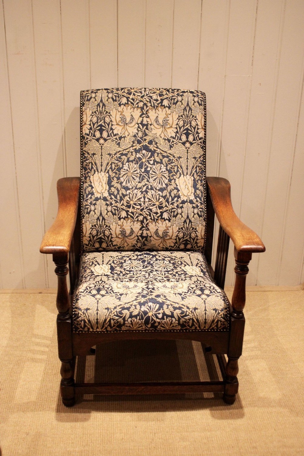 An Arts and Crafts oak reclining armchair featuring slatted sides, turned front legs, wide armrests, and floral pattern upholstery in blue and cream tones. View II