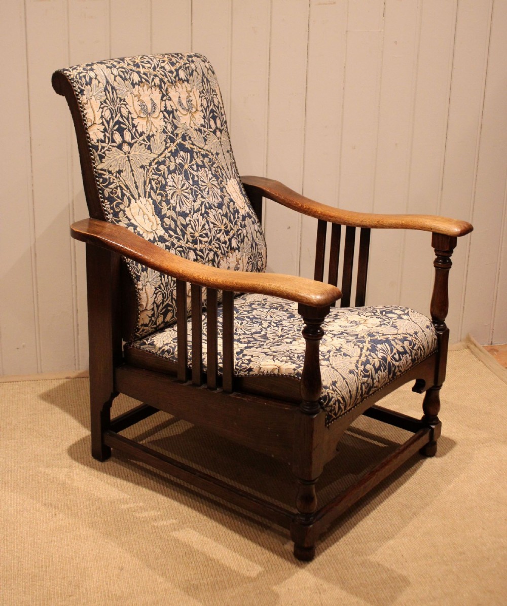 An Arts and Crafts oak reclining armchair featuring slatted sides, turned front legs, wide armrests, and floral pattern upholstery in blue and cream tones. View IV