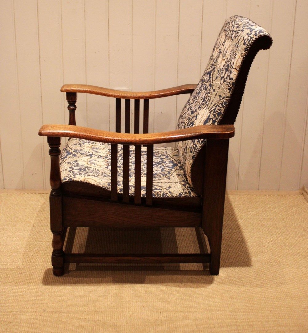 An Arts and Crafts oak reclining armchair featuring slatted sides, turned front legs, wide armrests, and floral pattern upholstery in blue and cream tones. View VI
