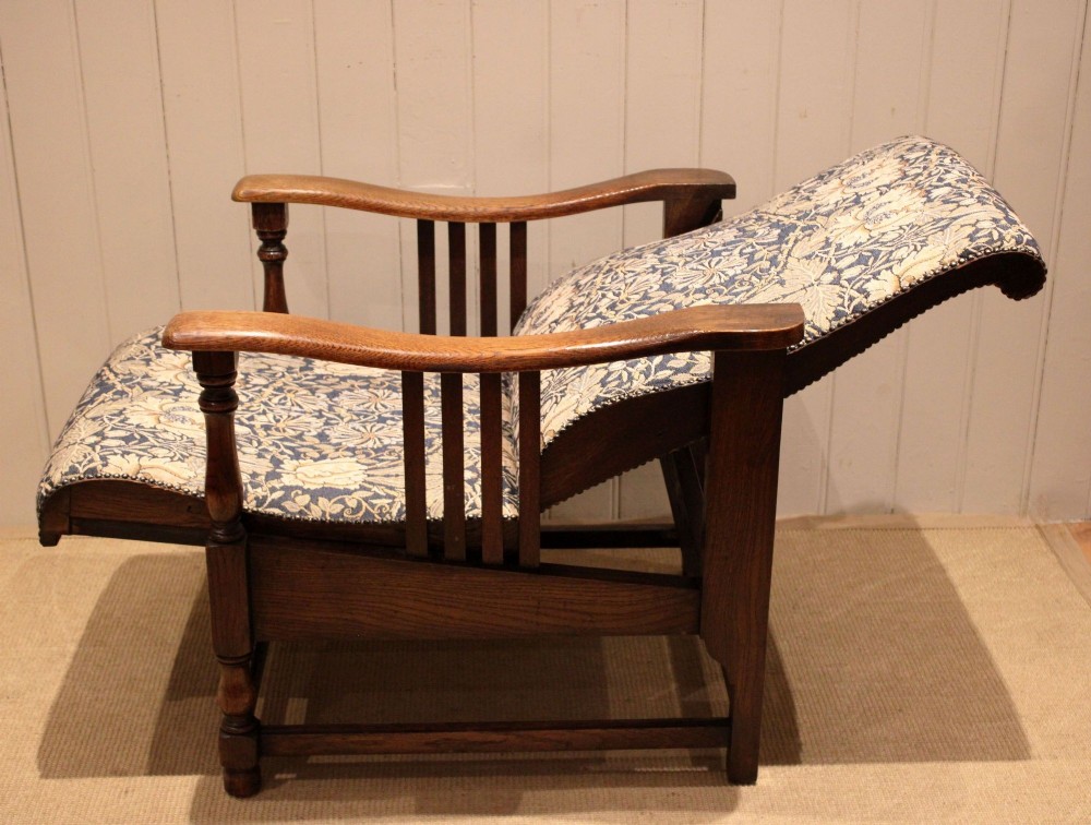 An Arts and Crafts oak reclining armchair featuring slatted sides, turned front legs, wide armrests, and floral pattern upholstery in blue and cream tones. View VII