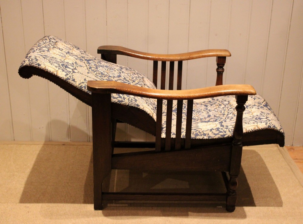 An Arts and Crafts oak reclining armchair featuring slatted sides, turned front legs, wide armrests, and floral pattern upholstery in blue and cream tones. View IX