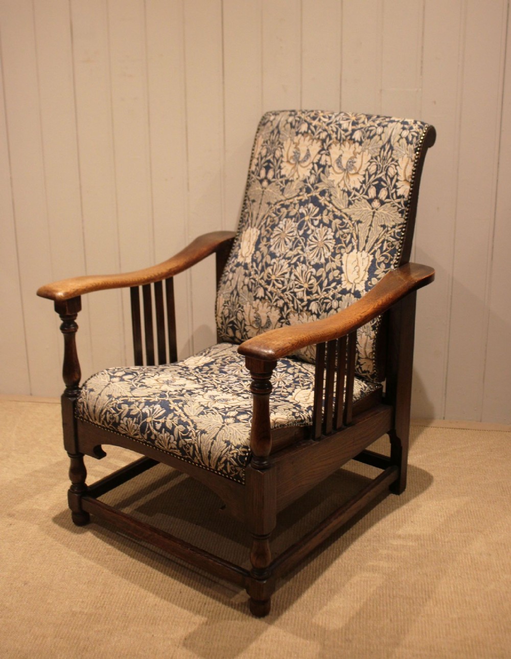 An Arts and Crafts oak reclining armchair featuring slatted sides, turned front legs, wide armrests, and floral pattern upholstery in blue and cream tones. View XI