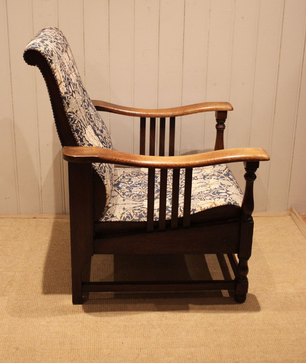 An Arts and Crafts oak reclining armchair featuring slatted sides, turned front legs, wide armrests, and floral pattern upholstery in blue and cream tones. View XII