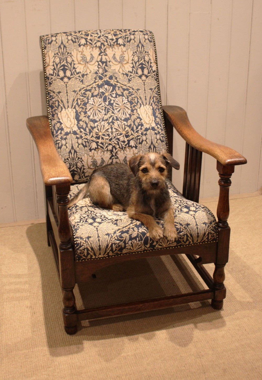 An Arts and Crafts oak reclining armchair featuring slatted sides, turned front legs, wide armrests, and floral pattern upholstery in blue and cream tones. View XV