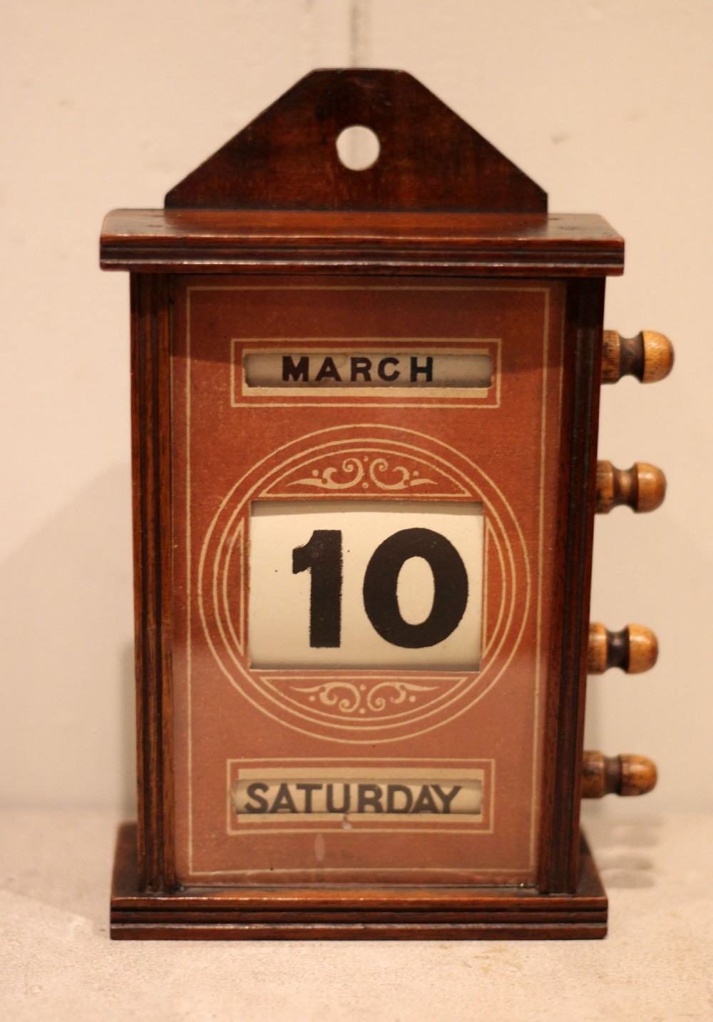 A late nineteenth-century mahogany perpetual desk calendar with turned wooden side knobs, displaying the date Saturday March 10.