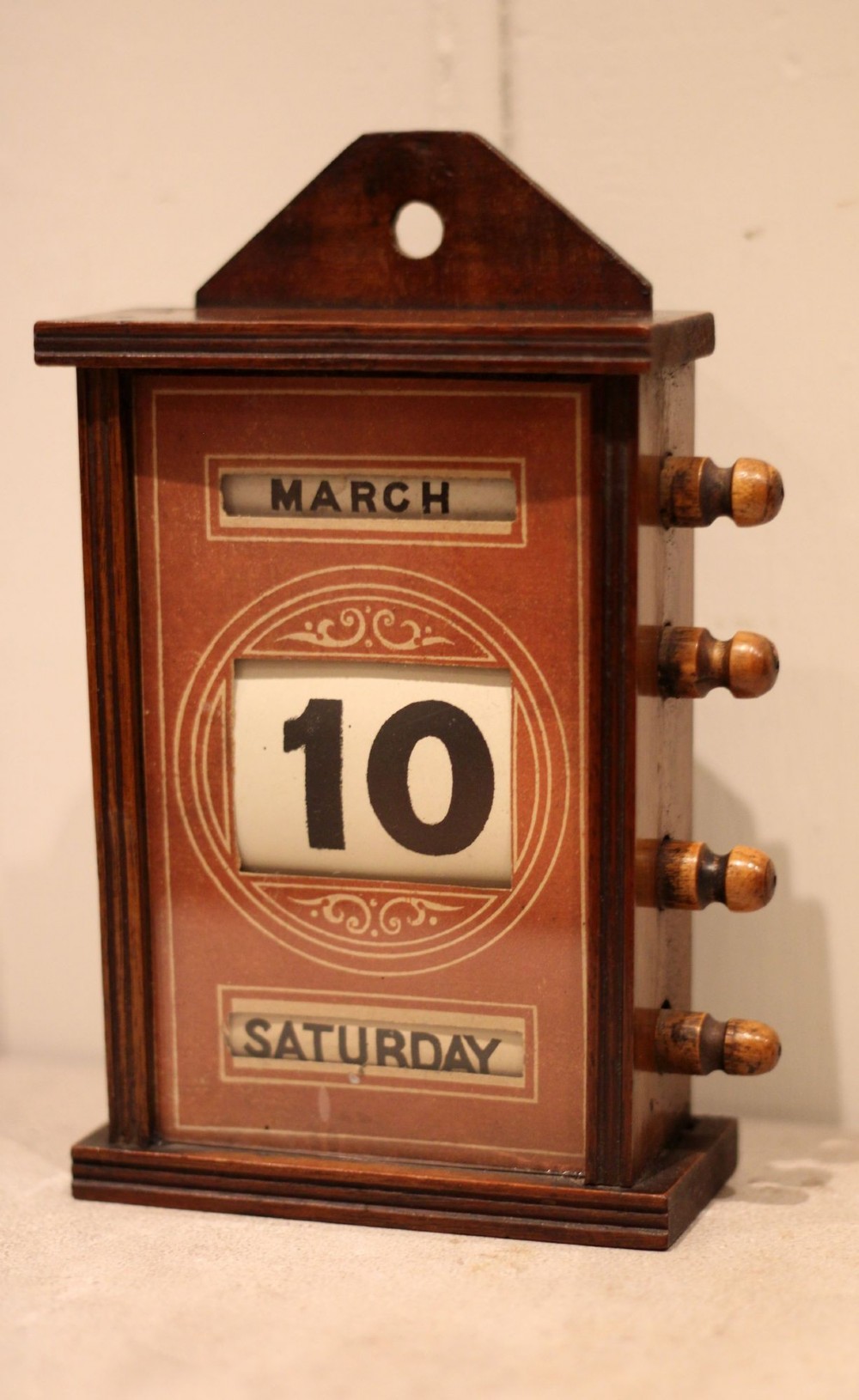 A late nineteenth-century mahogany perpetual desk calendar with turned wooden side knobs, displaying the date Saturday March 10. View IV