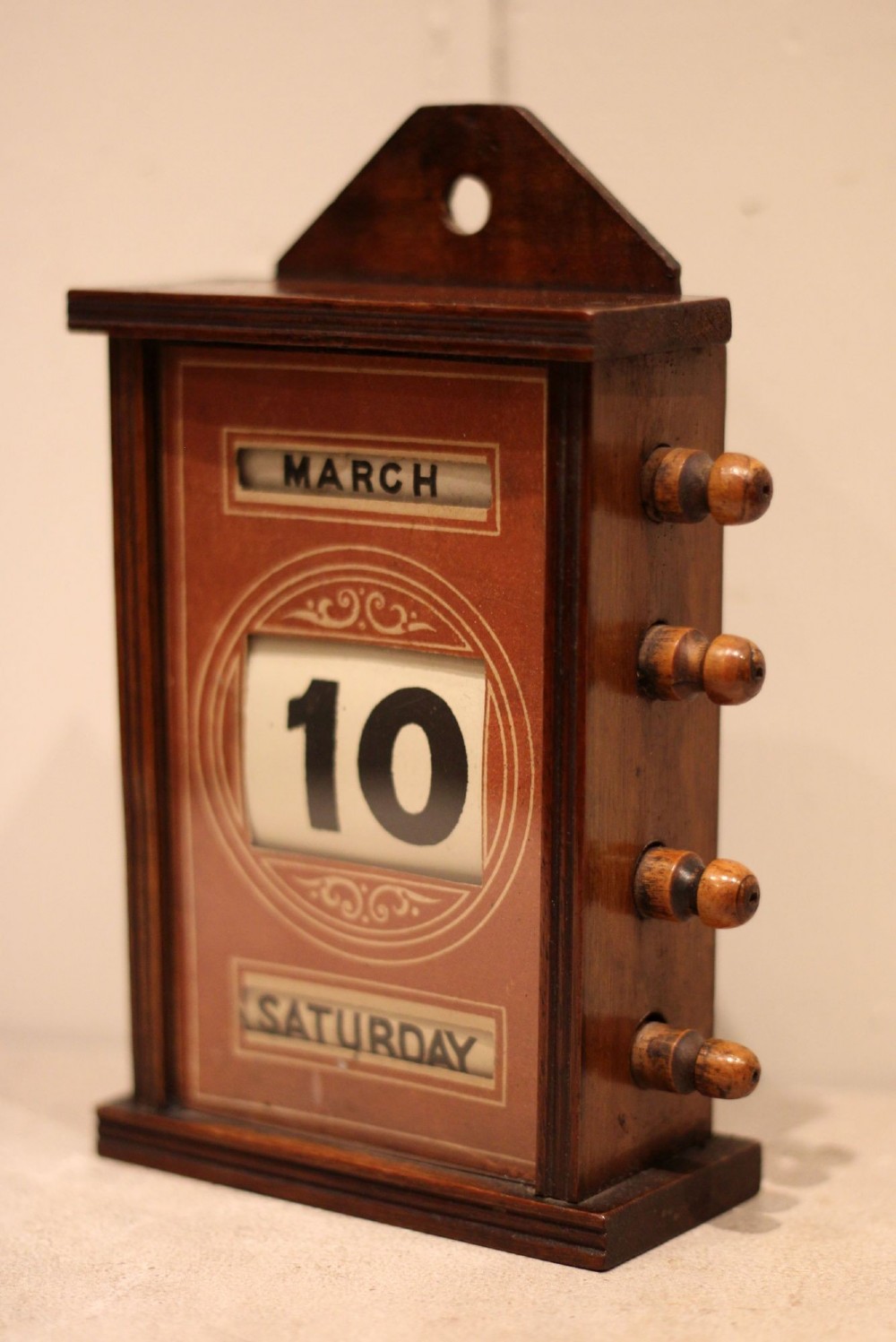 A late nineteenth-century mahogany perpetual desk calendar with turned wooden side knobs, displaying the date Saturday March 10. View VII