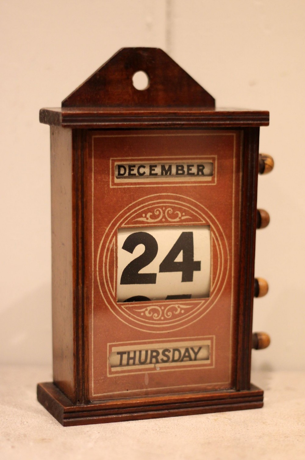 A late nineteenth-century mahogany perpetual desk calendar with turned wooden side knobs, displaying the date Saturday March 10. View VIII