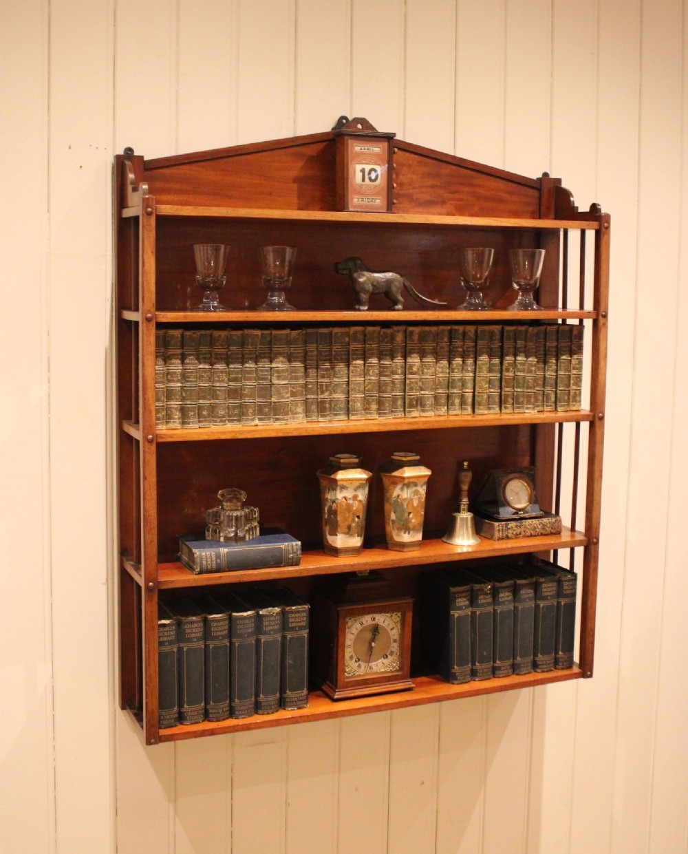 A four-tier mahogany wall-mounted shelving unit featuring open spindled sides and a peaked pediment top.
