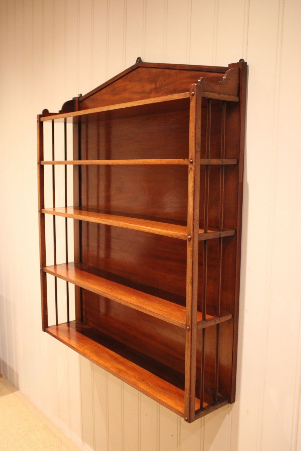 A four-tier mahogany wall-mounted shelving unit featuring open spindled sides and a peaked pediment top. View X