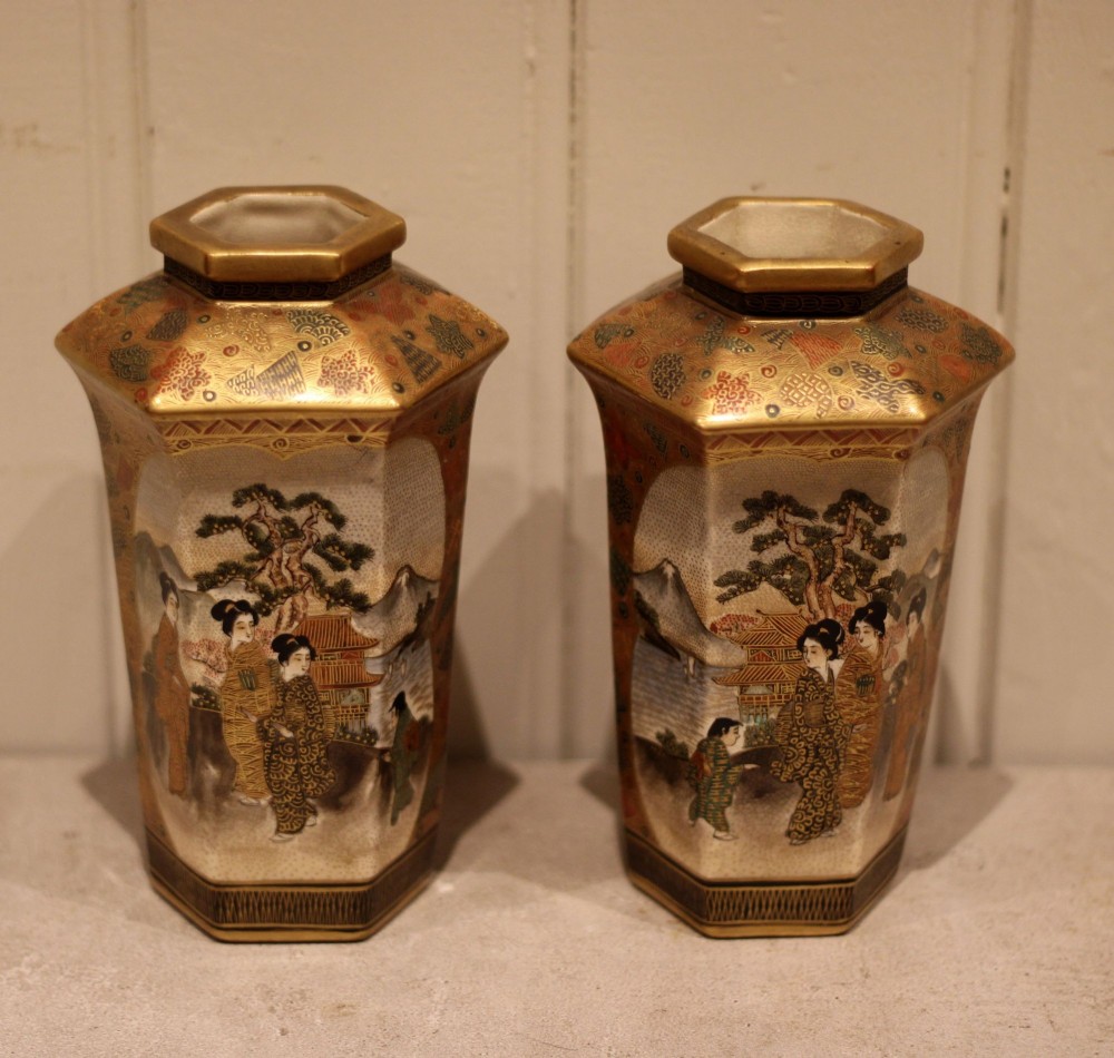 A pair of hexagonal Japanese Satsuma ceramic vases painted with figural scenes, mountain landscapes, and heavy gold enamel detailing.