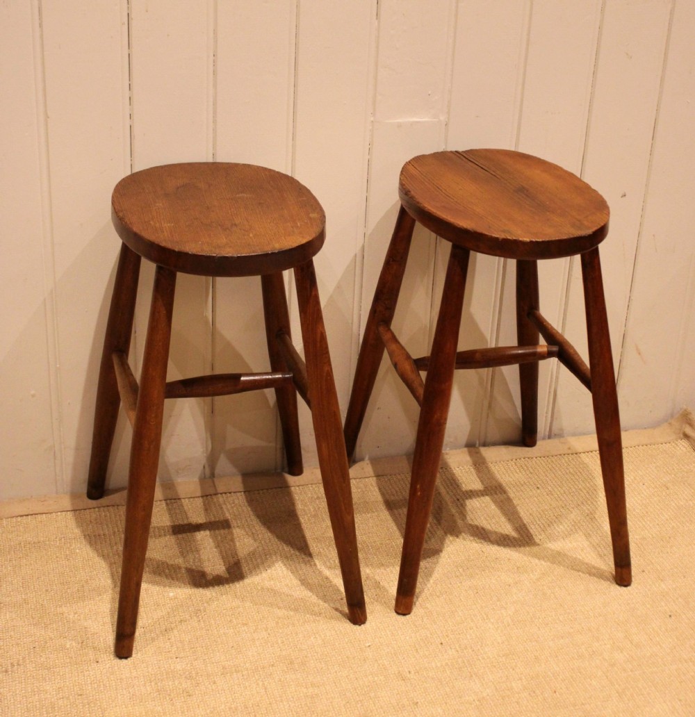 A pair of rustic warm brown wooden stools crafted with oval seats, turned splayed legs, and supporting stretchers.