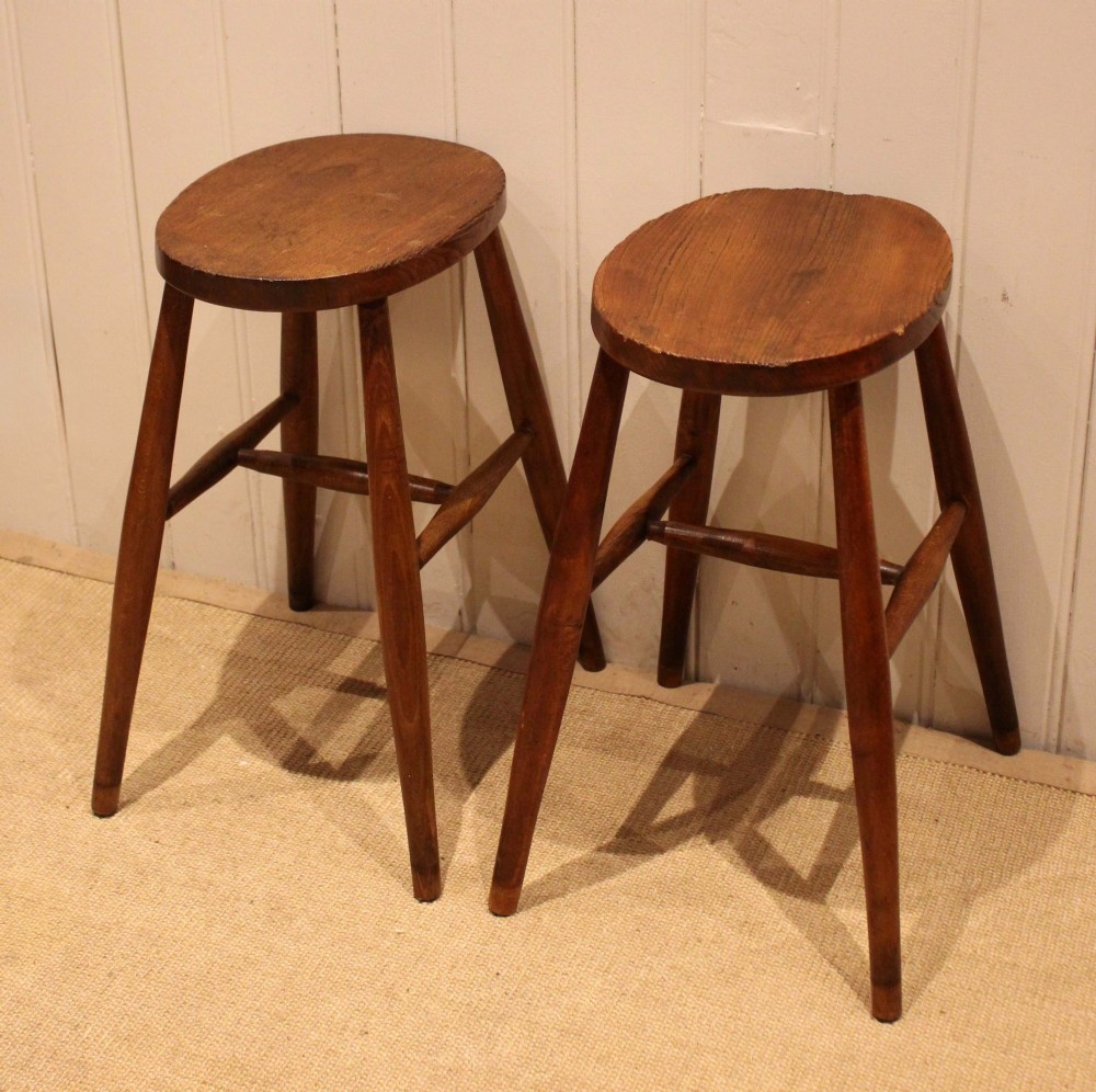 A pair of rustic warm brown wooden stools crafted with oval seats, turned splayed legs, and supporting stretchers. View II