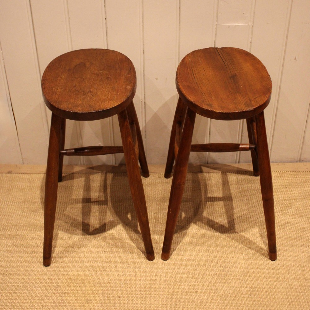 A pair of rustic warm brown wooden stools crafted with oval seats, turned splayed legs, and supporting stretchers. View III