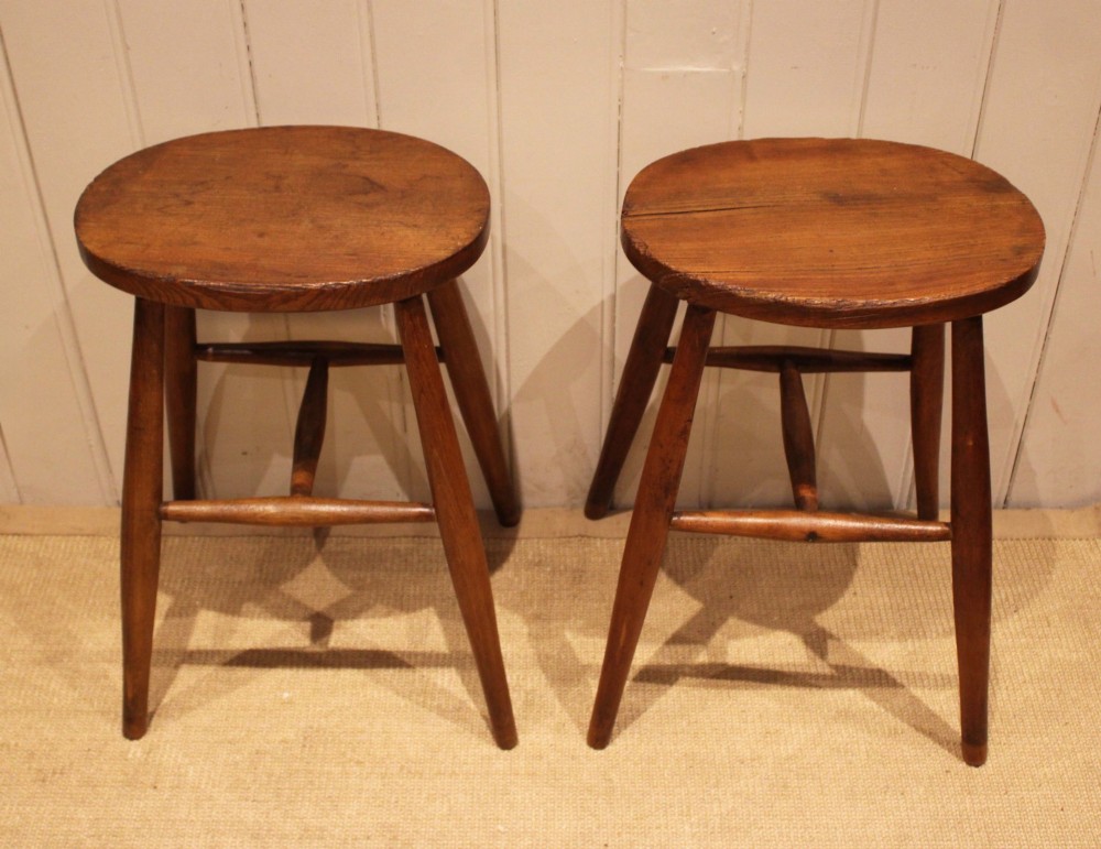A pair of rustic warm brown wooden stools crafted with oval seats, turned splayed legs, and supporting stretchers. View IV