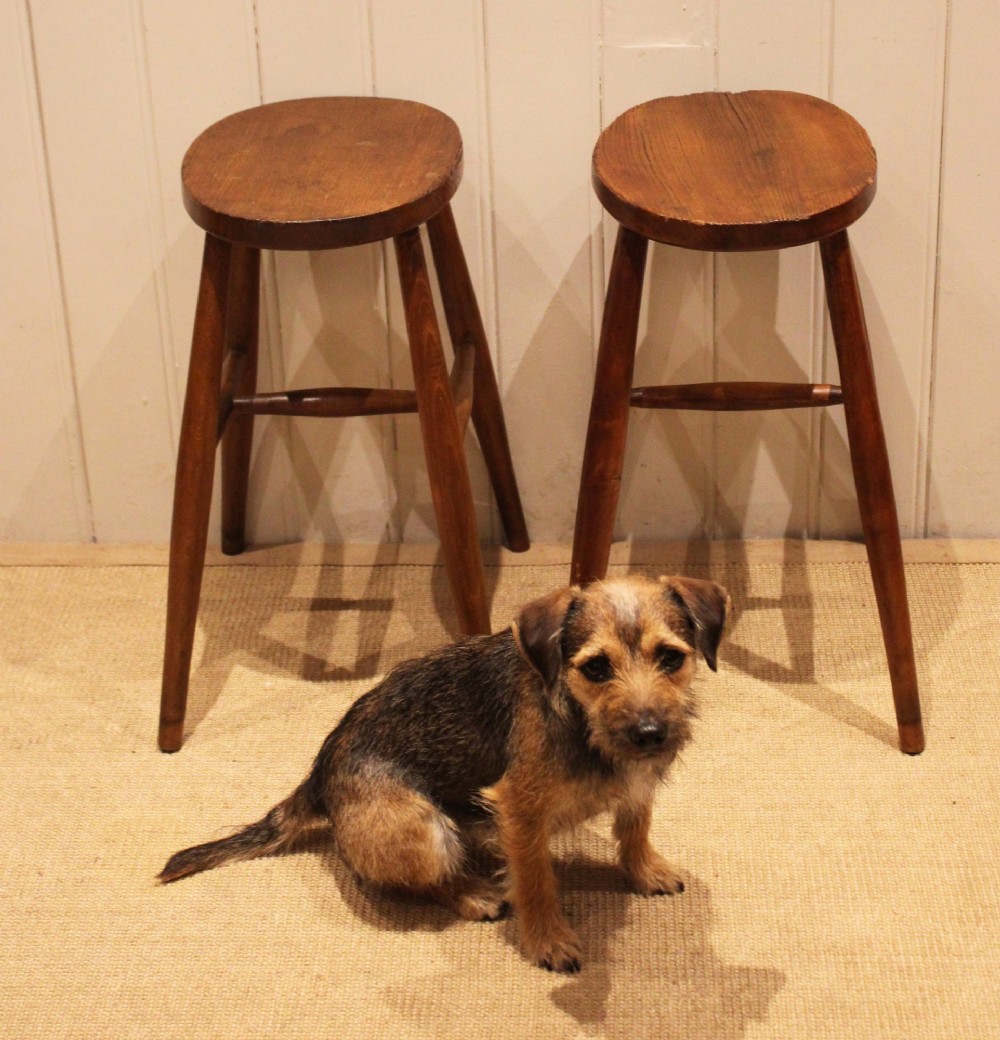 A pair of rustic warm brown wooden stools crafted with oval seats, turned splayed legs, and supporting stretchers. View V