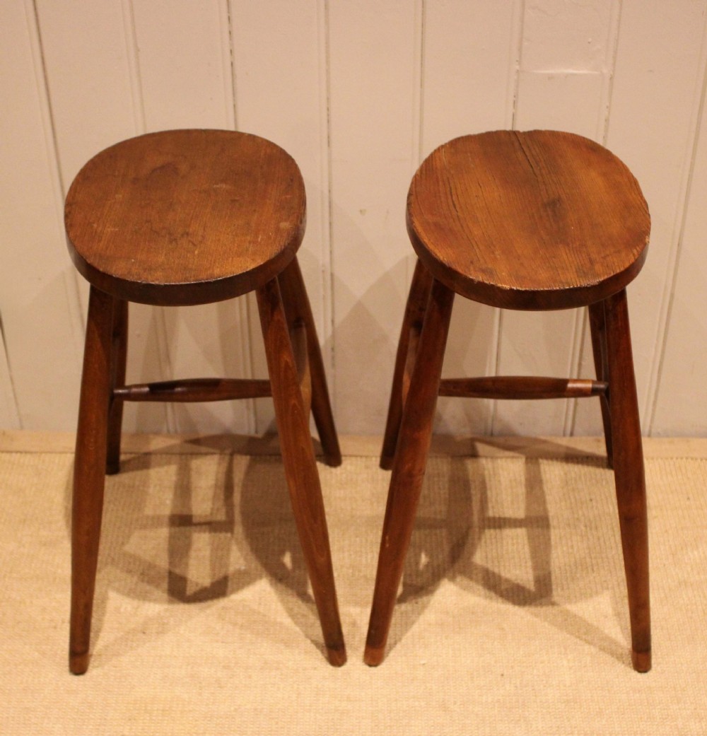 A pair of rustic warm brown wooden stools crafted with oval seats, turned splayed legs, and supporting stretchers. View VI