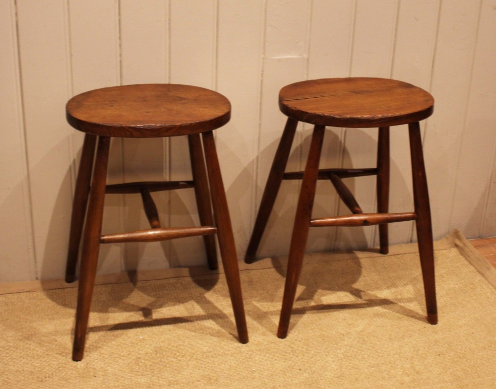 A pair of rustic warm brown wooden stools crafted with oval seats, turned splayed legs, and supporting stretchers. View VII