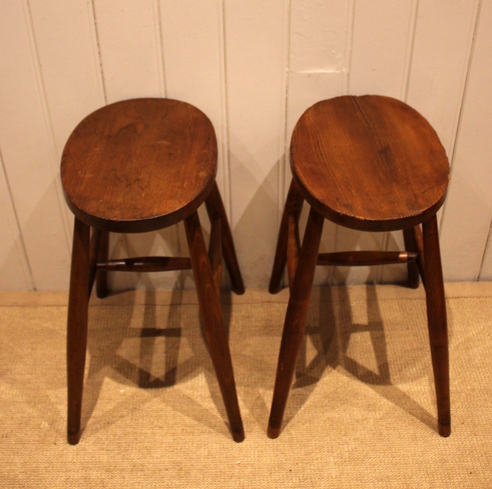 A pair of rustic warm brown wooden stools crafted with oval seats, turned splayed legs, and supporting stretchers. View VIII