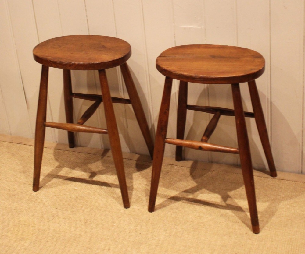 A pair of rustic warm brown wooden stools crafted with oval seats, turned splayed legs, and supporting stretchers. View IX