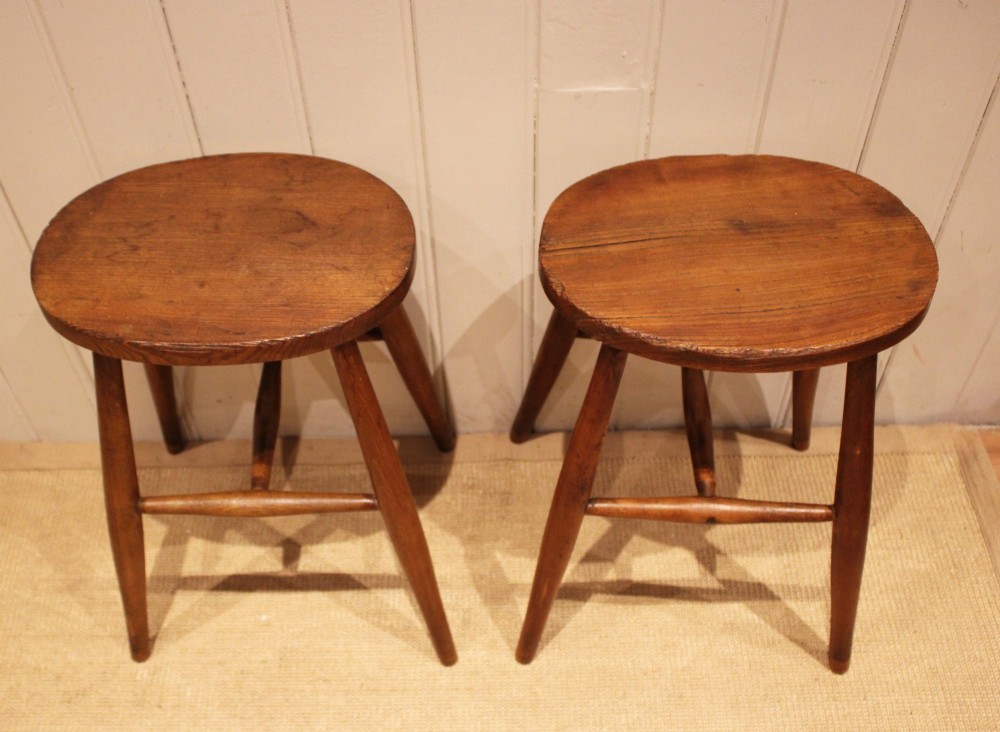 A pair of rustic warm brown wooden stools crafted with oval seats, turned splayed legs, and supporting stretchers. View XI