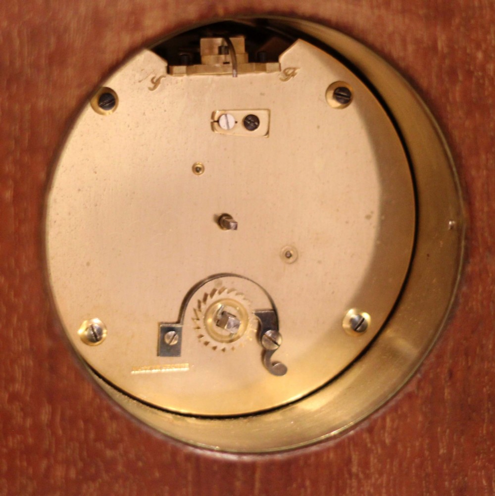 An Edwardian mahogany mantel clock featuring an arched wooden case, brass bezel, white circular dial with Roman numerals, and brass feet. View XI