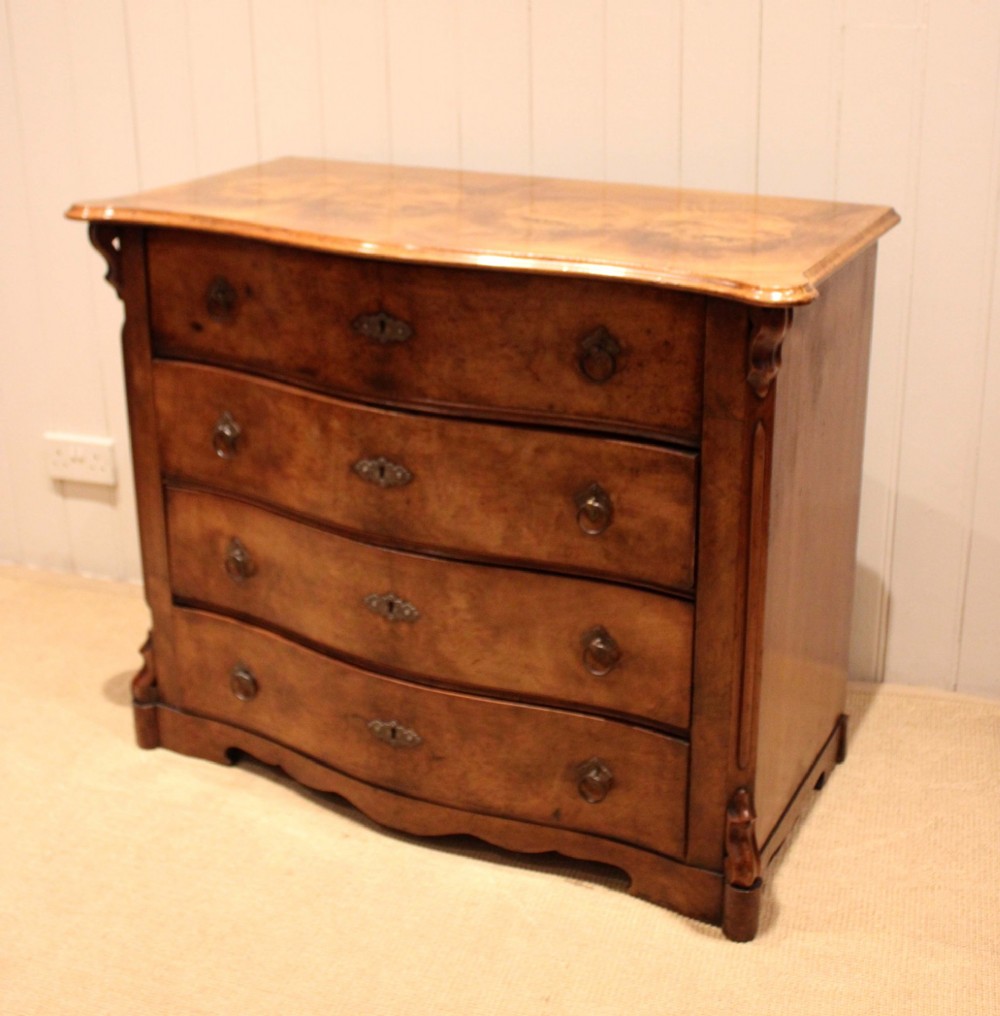 A mid-19th century burr walnut chest of four graduated drawers with a serpentine contoured front and brass drop handles. View IV