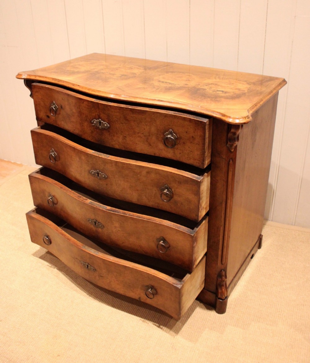A mid-19th century burr walnut chest of four graduated drawers with a serpentine contoured front and brass drop handles. View IX