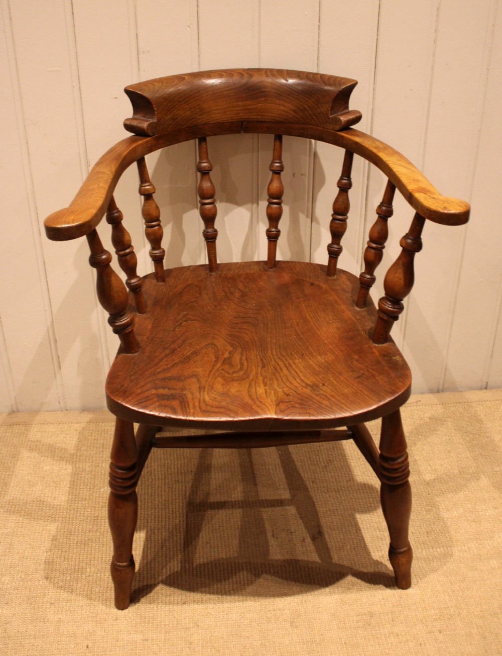 A late 19th-century wooden smokers bow armchair featuring a curved top rail, turned spindles, contoured saddle seat, and turned legs.