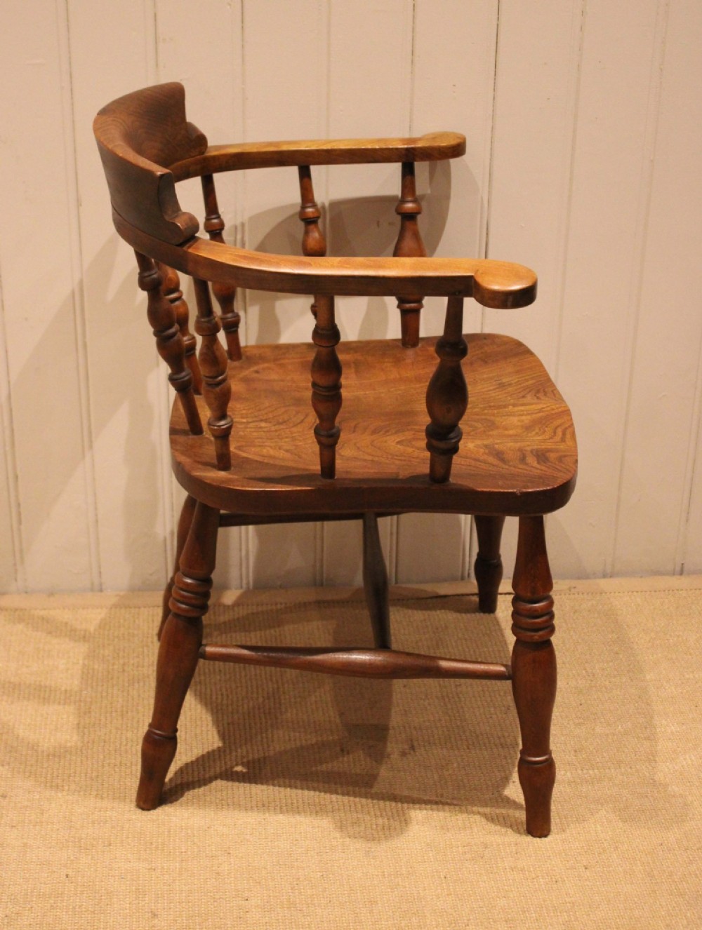 A late 19th-century wooden smokers bow armchair featuring a curved top rail, turned spindles, contoured saddle seat, and turned legs. View V