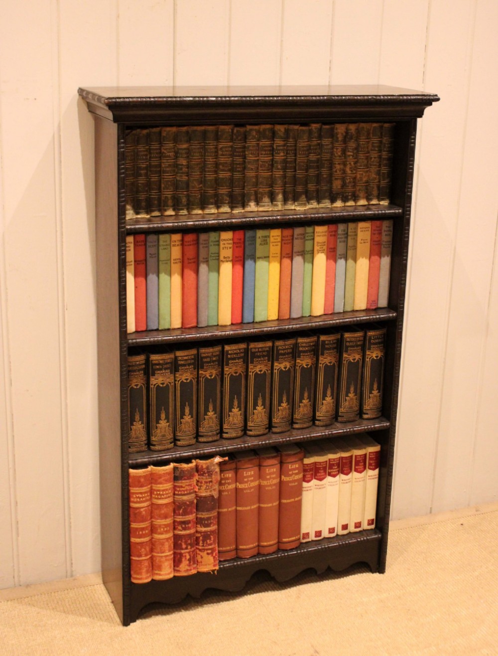 An antique dark oak open bookcase featuring four fixed shelves decorated with beaded edge mouldings and a shaped base plinth.