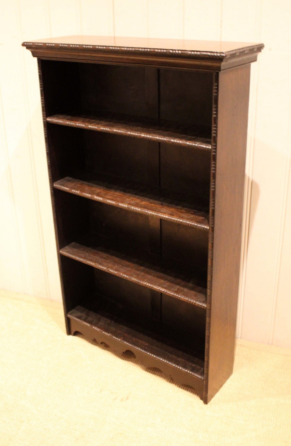 An antique dark oak open bookcase featuring four fixed shelves decorated with beaded edge mouldings and a shaped base plinth. View II
