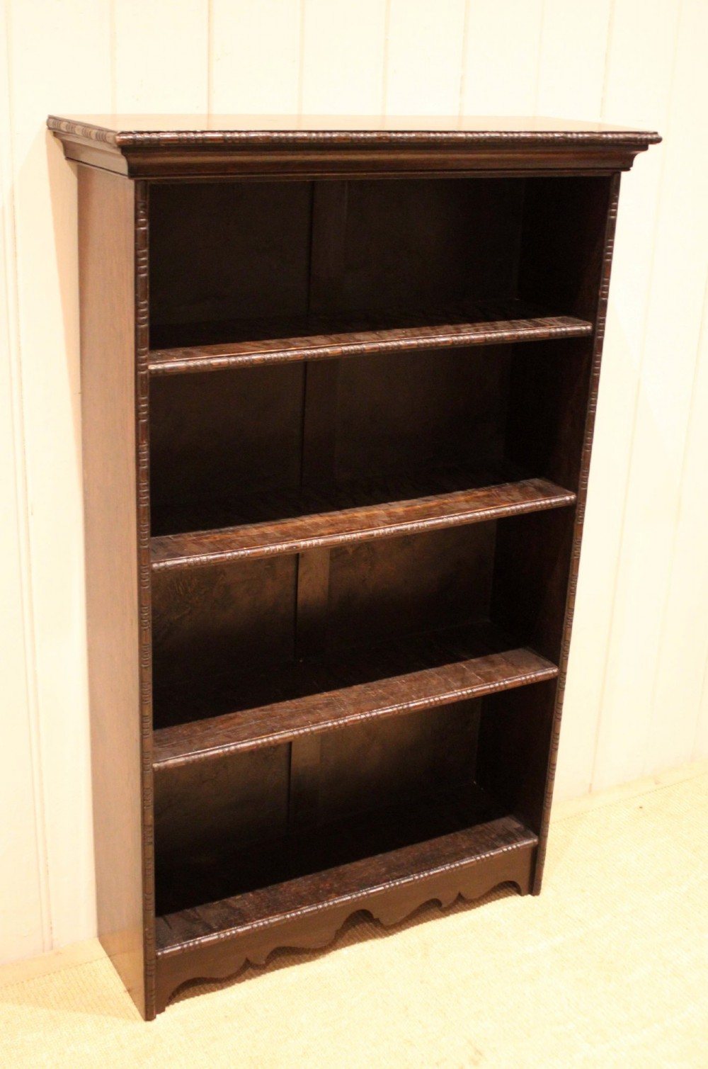 An antique dark oak open bookcase featuring four fixed shelves decorated with beaded edge mouldings and a shaped base plinth. View IV