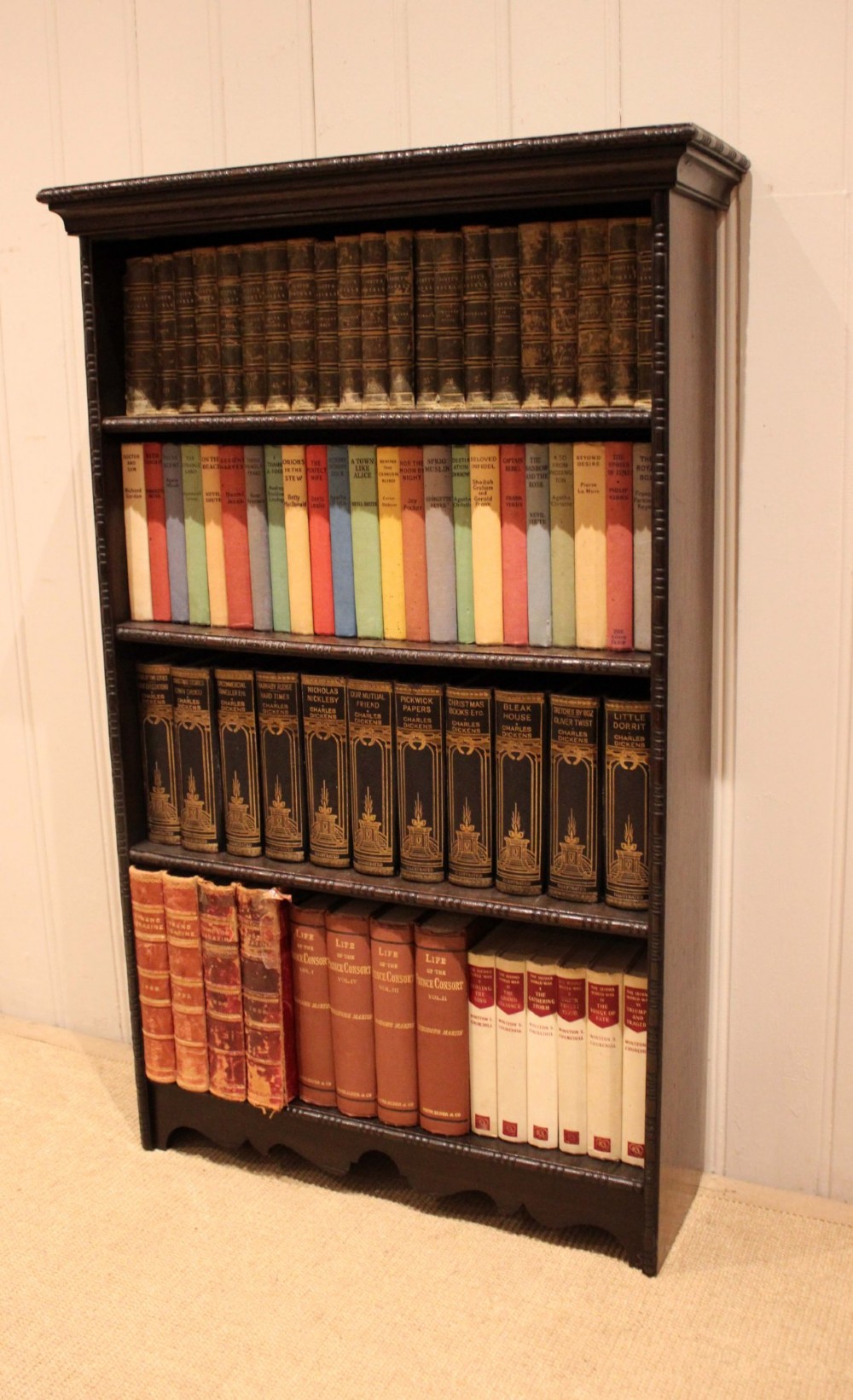 An antique dark oak open bookcase featuring four fixed shelves decorated with beaded edge mouldings and a shaped base plinth. View V