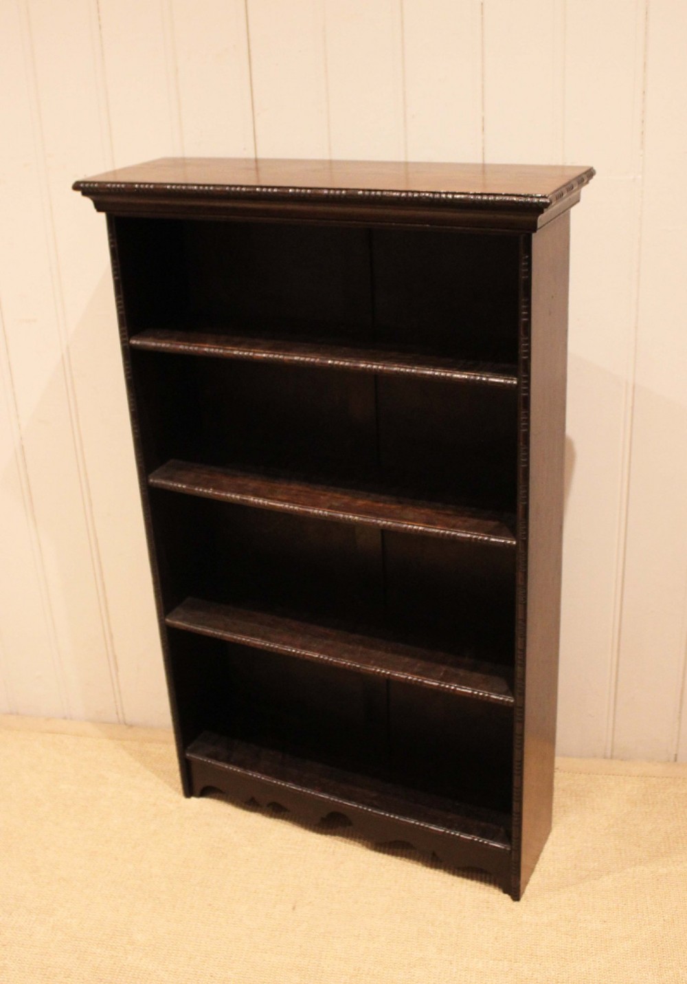 An antique dark oak open bookcase featuring four fixed shelves decorated with beaded edge mouldings and a shaped base plinth. View VI
