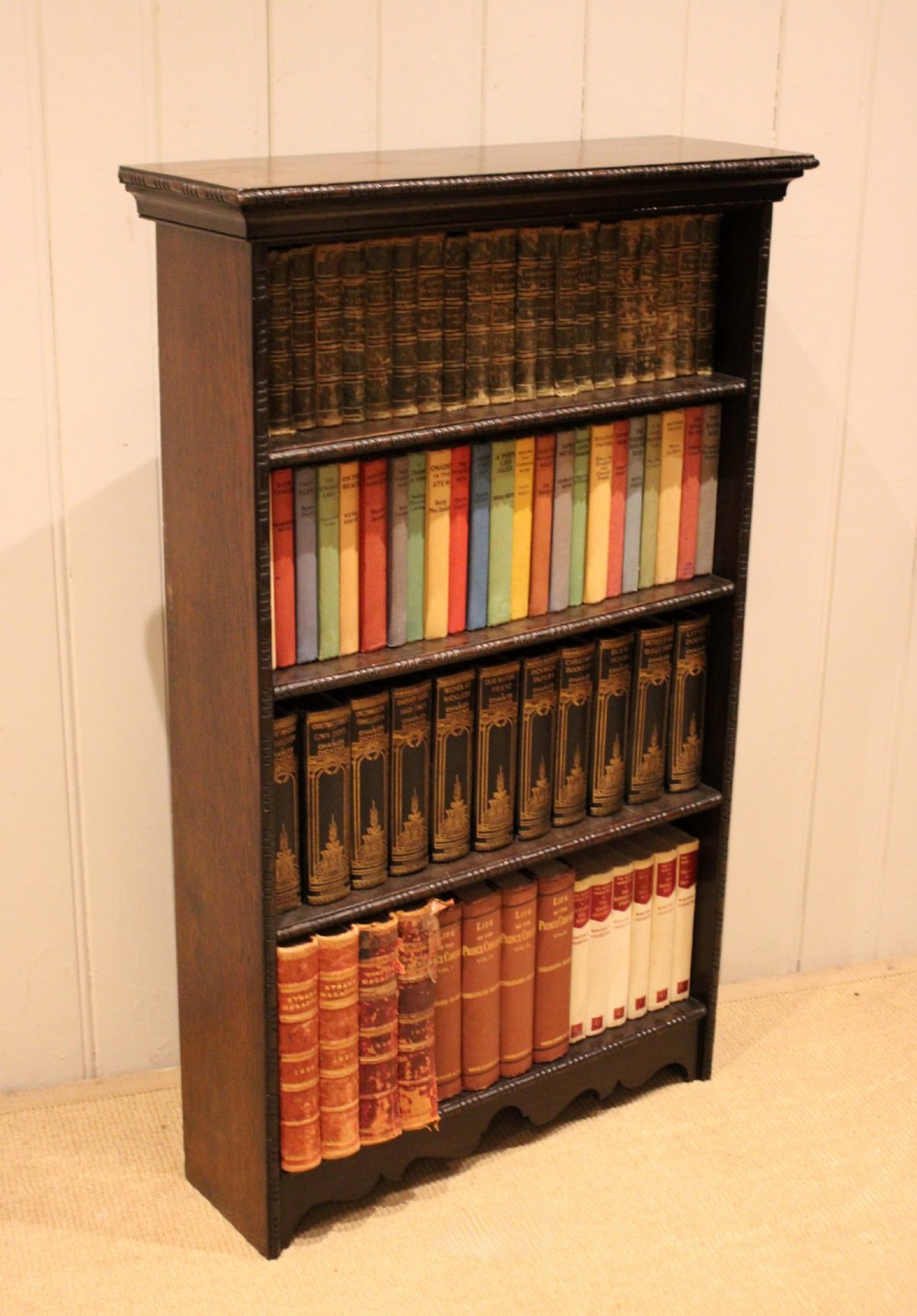 An antique dark oak open bookcase featuring four fixed shelves decorated with beaded edge mouldings and a shaped base plinth. View IX