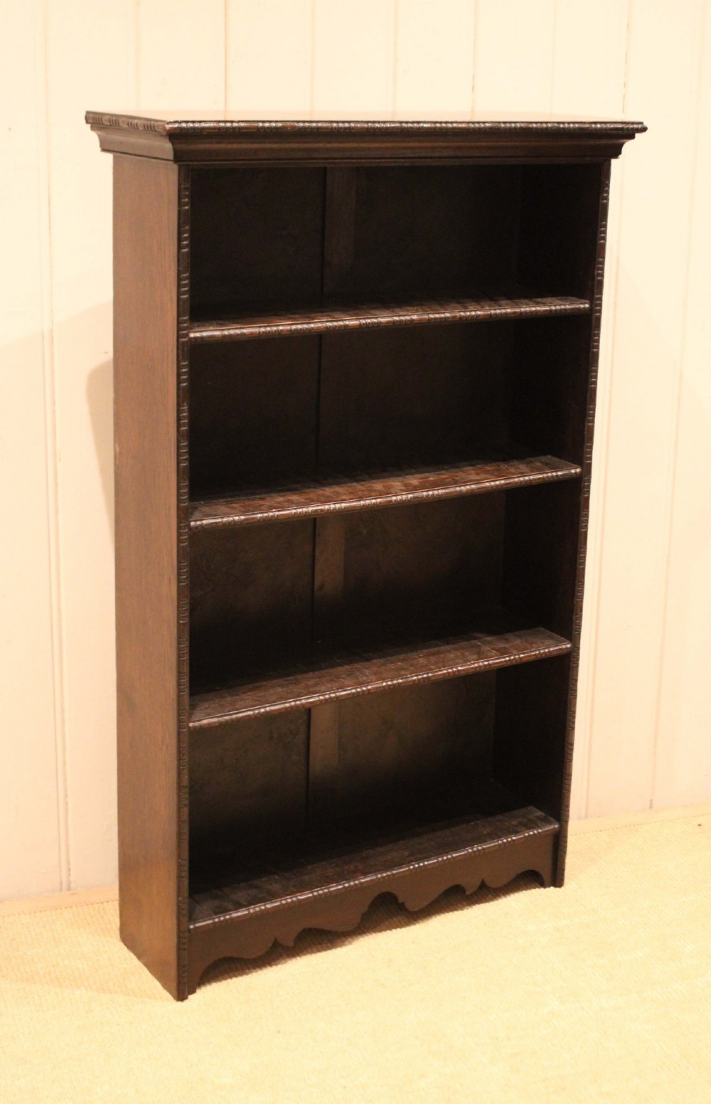 An antique dark oak open bookcase featuring four fixed shelves decorated with beaded edge mouldings and a shaped base plinth. View X