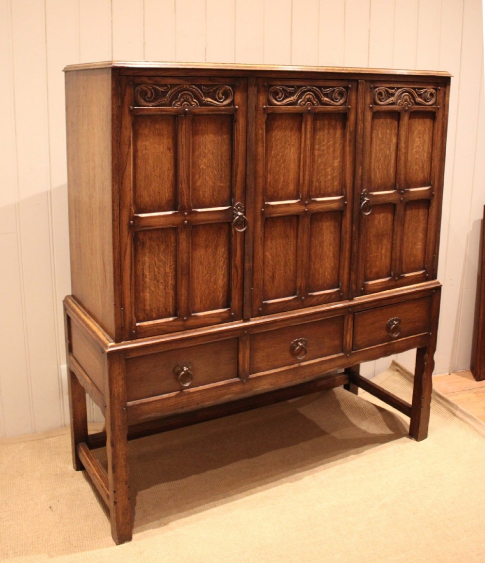 A solid oak side cabinet featuring three carved panel doors above three short drawers on square legs. View III