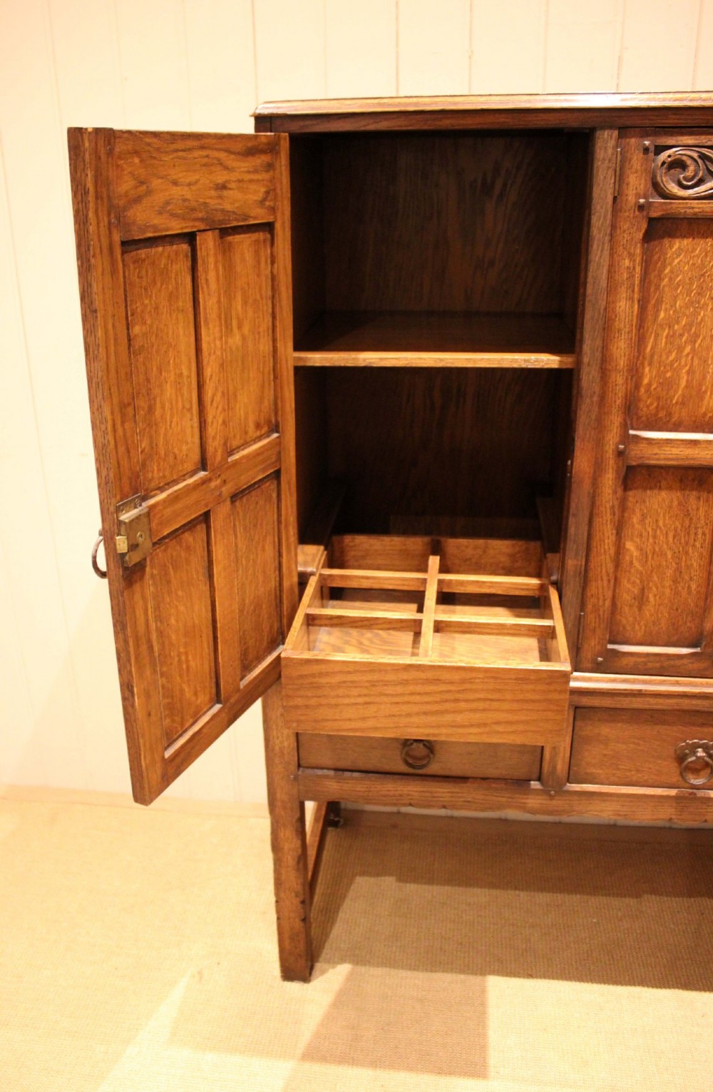 A solid oak side cabinet featuring three carved panel doors above three short drawers on square legs. View IV