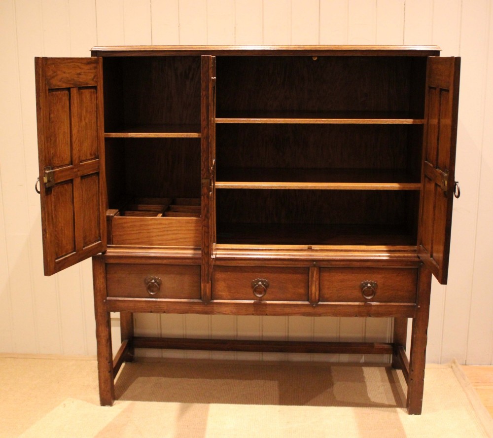 A solid oak side cabinet featuring three carved panel doors above three short drawers on square legs. View V