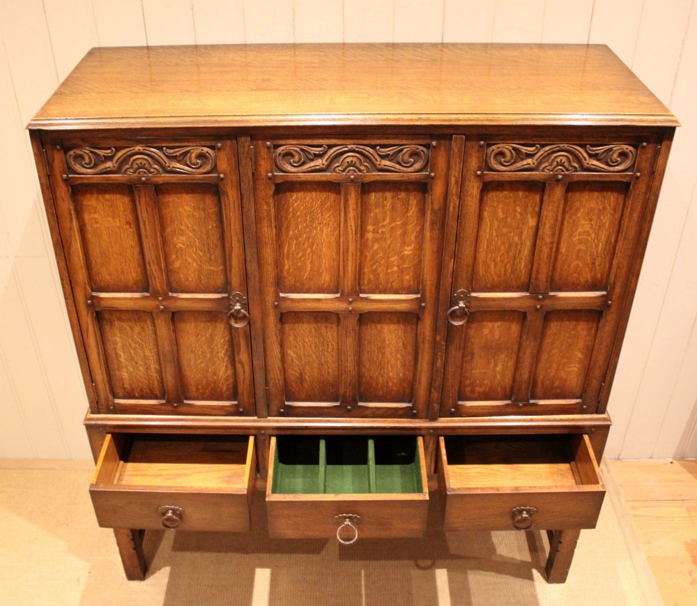 A solid oak side cabinet featuring three carved panel doors above three short drawers on square legs. View VI