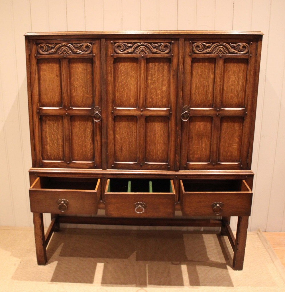 A solid oak side cabinet featuring three carved panel doors above three short drawers on square legs. View VII